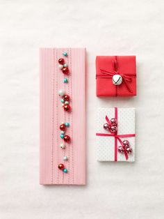 two pieces of pink paper with bows and beads on them, one is wrapped in red ribbon