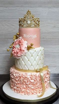 a three tiered cake with pink and gold decorations on the top, sitting on a plate