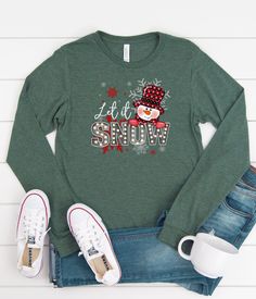 Get in the spirit of the Christmas season with this Let It Snow Snowman long sleeve graphic shirt. Perfect for Christmas morning or a day at the Christmas Tree Farm, or all winter long. This cute Christmas T-shirt is so adorable for your Christmas and winter festivities! Our shirts are great for the fall season and would make a great gift.  Are you looking for your new favorite t-shirt? Our graphic tees are custom created specifically for you and made by me not sourced out to a print shop. Selec Winter Holiday Long Sleeve T-shirt, Winter Long Sleeve Graphic Shirt, Winter Holiday Long Sleeve Tops, Festive Long Sleeve Holiday T-shirt, Winter Festive Long Sleeve Tops, Holiday Long Sleeve Top With Graphic Print, Festive Winter Crew Neck Shirt, Long Sleeve Graphic Print Top For Holiday, Christmas Festive Long Sleeve Tops