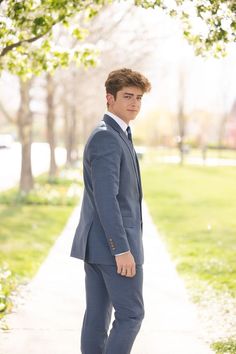 a young man in a suit and tie standing on a sidewalk next to a tree