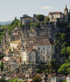 an old castle perched on top of a cliff in the middle of a town surrounded by trees