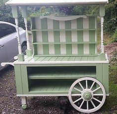 a green and white cart with wheels on the ground next to a car in front of it