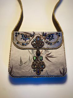 "This jeweled purse is %100 handmade. The main body features Chinese silk with floral patterns, Chinese frog closures, beading, and iridescent jewels. The strap and side/bottom are of French silk brocade with gold braid trimming. The inside is lined with Chinese silk with elaborate dragon patterns and features a small, open top pocket for handy access to smaller items.  Measurements:  Main: 8.5\" wide, 7\" height, 2.5\" deep Inside pocket: 5\" wide, 4\" height Strap length: 3' Strap height from top of purse to apex of mid strap as when worn: 16\" Must be handled delicately. Please note: the colors of some pictures may vary slightly on different monitors." Designer Embroidered Gold Shoulder Bag, Designer Gold Embellished Shoulder Bag, Designer Gold Embroidered Shoulder Bag, Formal Hand Embellished Shoulder Bag, Embellished Rectangular Shoulder Bag For Evening, Luxury Hand Embellished Shoulder Bag For Formal Occasions, Gold Shoulder Bag With Handwork For Evening, Gold Evening Shoulder Bag With Handwork, Designer Handmade Evening Shoulder Bag