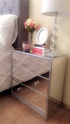 a mirrored nightstand sitting next to a bed with a white comforter on top of it