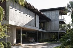 a car is parked in front of a house with palm trees and other greenery