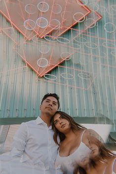 a man and woman sitting next to each other in front of a neon sign with circles on it