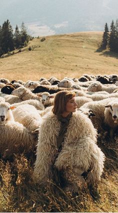 a woman sitting in the middle of a herd of sheep