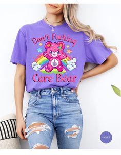 Indulge in rebellious comfort with our "I Don't Care Bear Vibes" T-shirt! This whimsical tee features a cheeky care bear boldly expressing your carefree attitude with a pair of unmistakable middle fingers and a vibrant rainbow backdrop. Crafted from soft, breathable fabric, this shirt guarantees both style and comfort. Embrace the carefree spirit and make a statement with this playful addition to your wardrobe. It's not just a shirt; it's an expression of your "don't give a care" attitude! *Unisex Sizing* Trendy Crew Neck T-shirt With Bear Print, Trendy Purple Slogan T-shirt, Casual Purple T-shirt With Cartoon Print, Cute Purple Relaxed Fit T-shirt, Cute Short Sleeve T-shirt With Bear Print, Fun Purple T-shirt With Funny Print, Cute Bear Print Crew Neck T-shirt, Graphic Tee With Bear Print And Crew Neck, Bear Print Crew Neck T-shirt For Streetwear