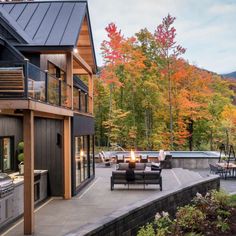 an outdoor kitchen and living room area in front of a mountain house with fall foliage