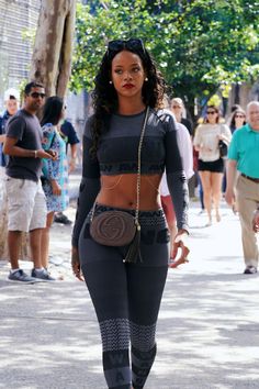 a woman is walking down the street in tight pants and crop top with an embellished purse