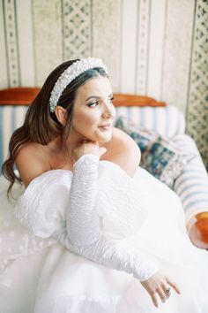 a woman in a white dress sitting on a couch wearing a tiara and holding her hand to her chin