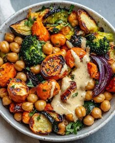 a bowl filled with broccoli, carrots and chickpeas covered in sauce