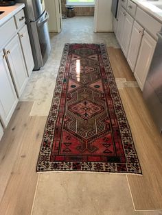 a red rug is in the middle of a kitchen with white cabinets and stainless steel appliances