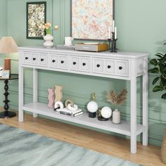 a white console table with three drawers and two candles on it in front of a green wall