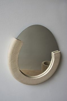 a circular mirror mounted to the side of a white wall next to a wooden shelf