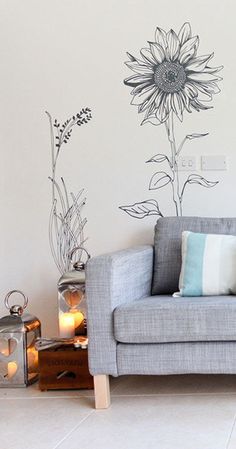 a grey couch sitting next to a wall with a sunflower painted on the wall