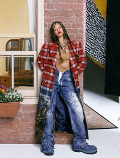 a woman leaning against a brick wall with her hands on her hips and wearing jeans