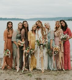 a group of women standing next to each other on a beach holding bouquets and flowers