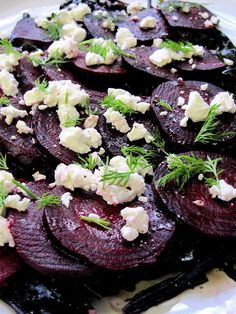 a white plate topped with sliced up beets covered in feta cheese and herbs