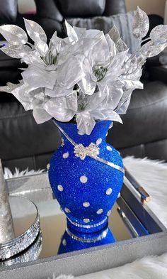 a blue vase filled with white flowers sitting on top of a glass table next to a black couch