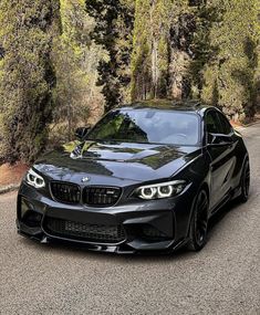 a black car is parked on the side of the road in front of some trees