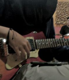 a man is playing an electric guitar while another person sits in the background