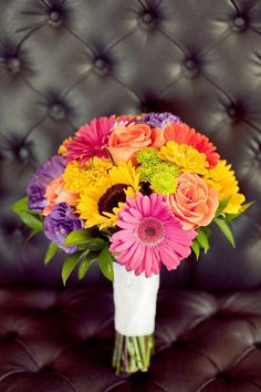 a vase filled with colorful flowers on top of a leather couch next to a black chair