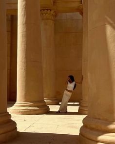 a woman standing in between two large pillars with her hand up to the ground,