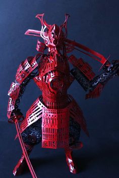 a red paper cut sculpture of a samurai holding two swords and wearing armor with intricate patterns