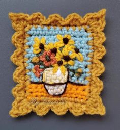 a crocheted square with flowers and a vase on the front is shown in yellow, blue, and orange