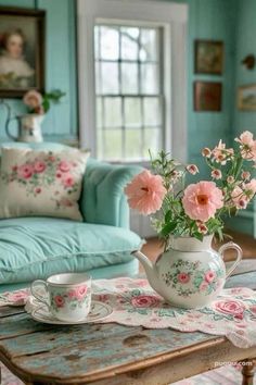 pink flowers in a teapot on a table with two cups and saucers next to it