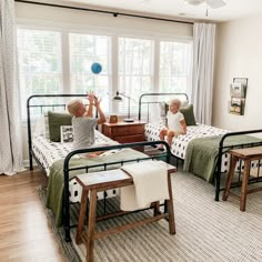 two children sitting on twin beds in a room with wood flooring and white walls