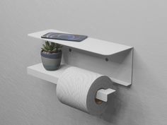 a toilet paper holder with a phone on the shelf above it and a plant next to it