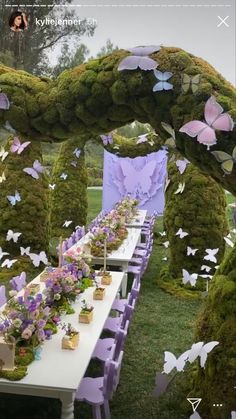 a long table covered in purple flowers and moss with butterfly decorations on it's sides