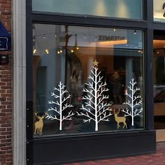 a store window with white trees and deer on it's windowsill, in front of a brick building