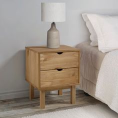 a nightstand with two drawers and a lamp on top of it next to a bed