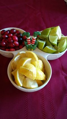 two bowls filled with fruit sitting on top of a red table cloth next to another bowl full of fruit