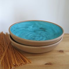 two blue bowls sitting next to each other on top of a wooden table with straws