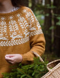 a woman holding a wicker basket and wearing a brown sweater with white designs on it