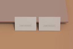 two square business cards sitting on top of a wooden table next to each other in front of a brown wall