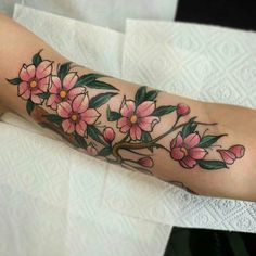 a woman's arm with pink flowers on it and green leaves in the middle