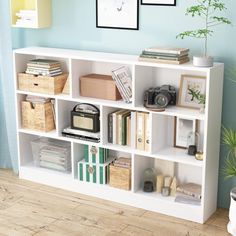 a white book shelf filled with books next to a plant and pictures on the wall