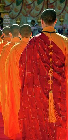 a group of monks in orange robes walking down a red carpet