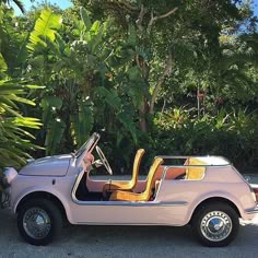 an old pink car parked in front of some trees and bushes with the door open