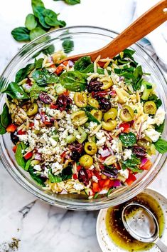 a salad in a glass bowl with a wooden spoon on the side and olives