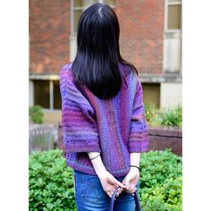 a woman with long black hair wearing a purple sweater and blue jeans holding a purse