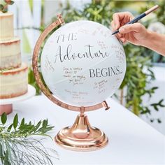 a person is writing on a globe at a table with flowers and greenery in the background