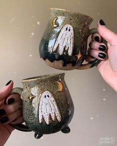 two hand painted mugs with ghost faces on them, one is holding the other