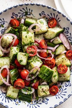 a bowl filled with cucumber, tomatoes and onions on top of a table