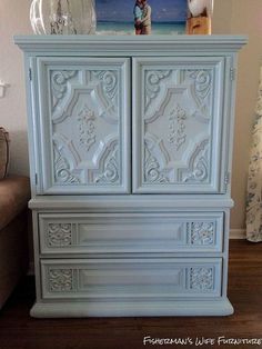 a white cabinet with an ornate design on it's doors and drawers, in a living room